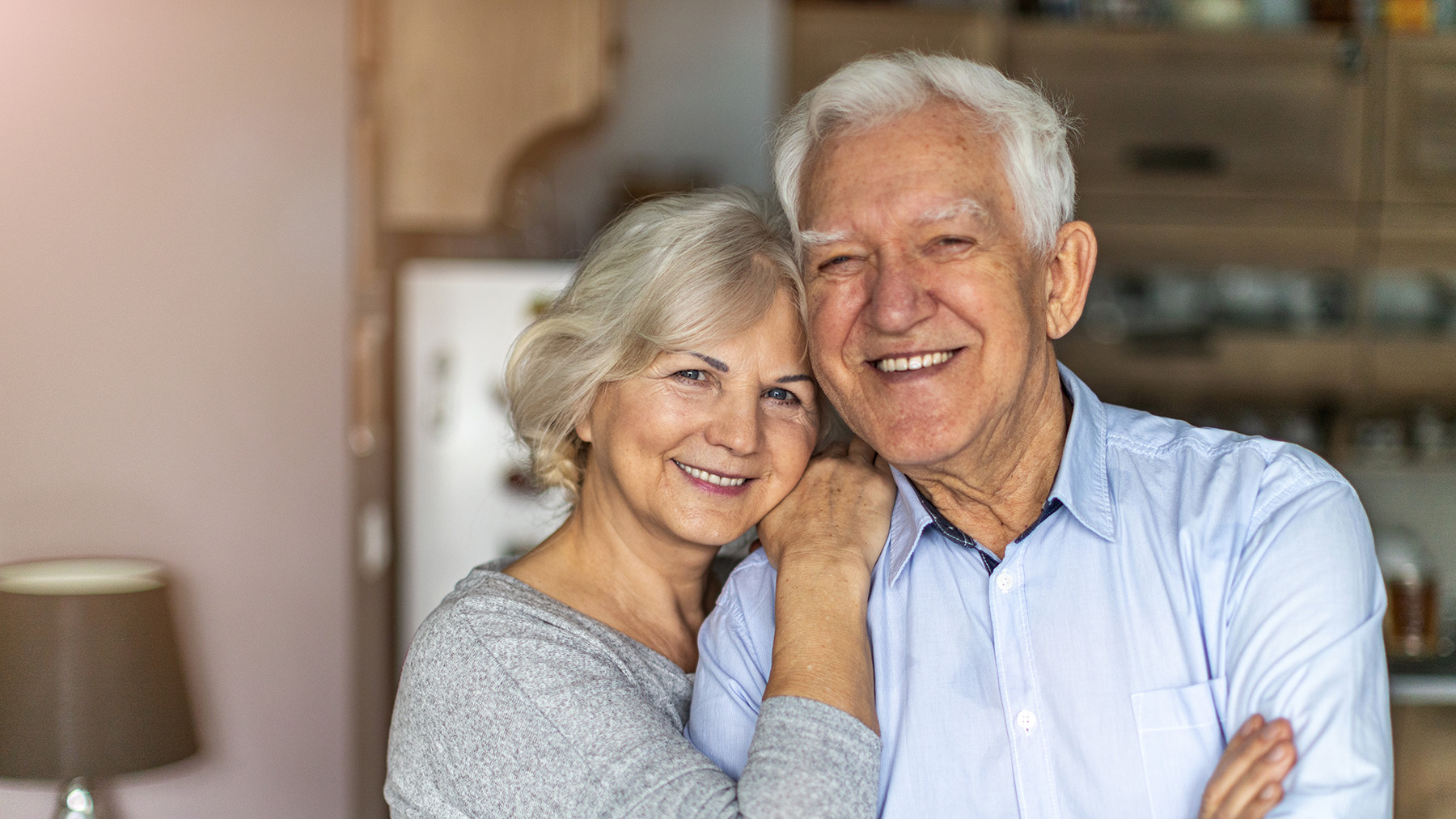 The image shows an older man and woman standing close together, smiling at the camera.