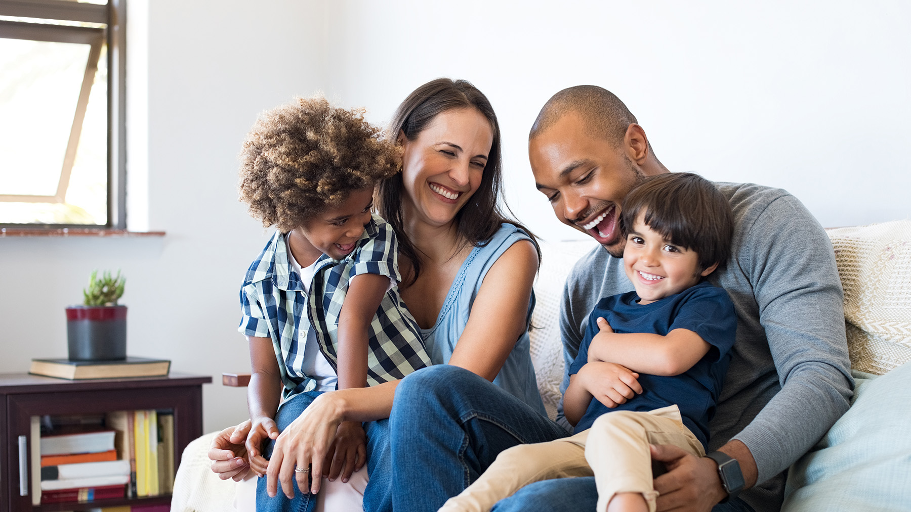 A family of four with two adults and two children gathered on a couch, smiling and looking towards the camera.